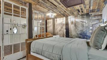 Ein Schlafzimmer mit Holzboden, einem Bett mit grauer Decke und einem großen Fenster mit Blick auf Bäume.