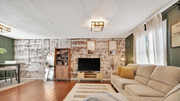 A living room with a brick wall, a flat-screen TV, a sofa, and a wooden cabinet. - Swann Ave Suite Walk to Bayshore Hyde Park (Tampa)