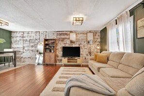 A living room with a brick wall, a flat-screen TV, a sofa, and a wooden cabinet. - Swann Ave Suite Walk to Bayshore Hyde Park (Tampa)