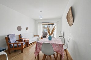 Ein Zimmer mit einem Bett, einem Esstisch mit Stühlen, einer blauen Vase und einer Hängeleuchte.