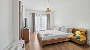A modern bedroom with a wooden bed, a bedside lamp, a TV, and a window with curtains. - Apartment 'Ocean Terrace 3 B - With Pool' with Swimming Pool and Balcony (Armação de Pêra)