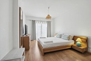 Ein modernes Schlafzimmer mit einem hölzernen Bett, einer Nachttischlampe, einem Fernseher und einem Fenster mit Vorhängen.