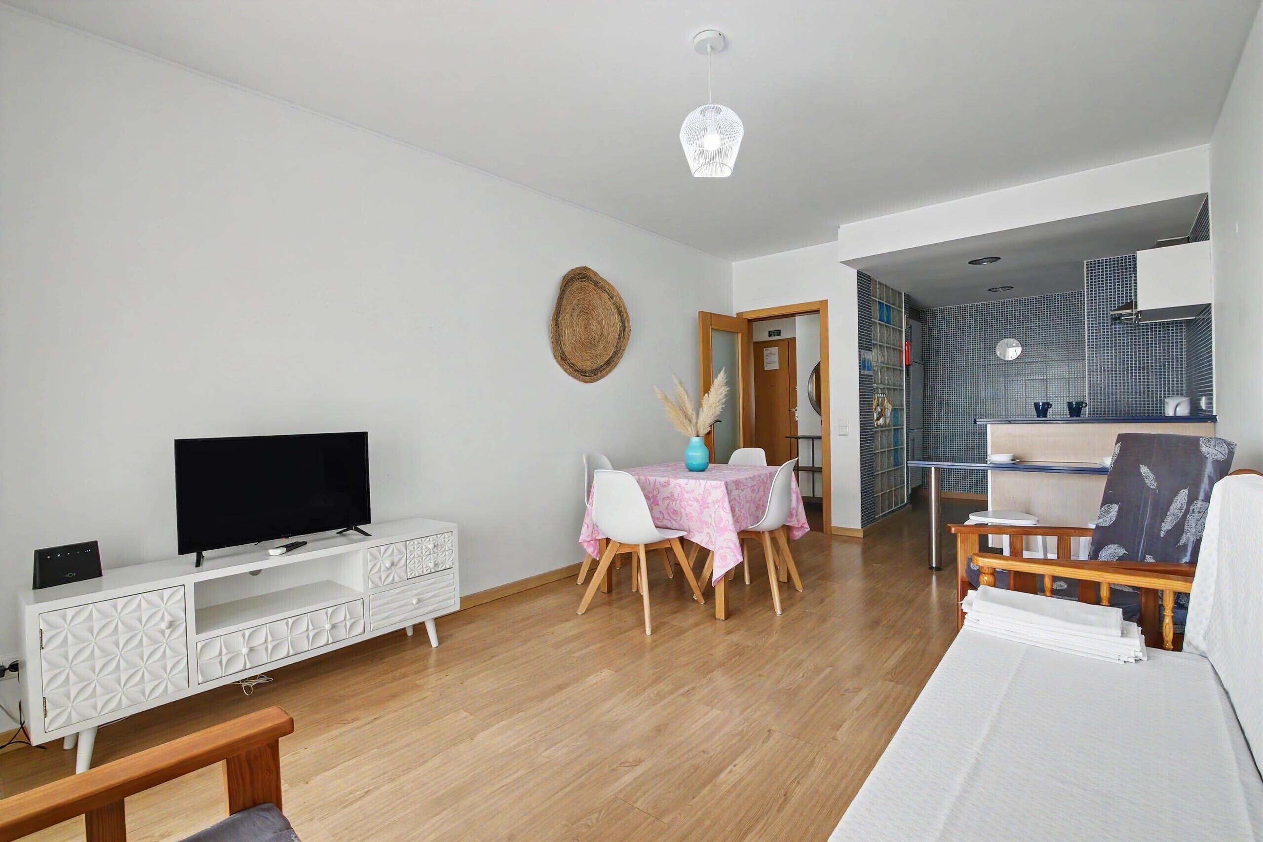 Ein modernes Wohnzimmer mit Flachbildfernseher, einem Esstisch mit Stühlen, einer Couch und einer Küche im Hintergrund.