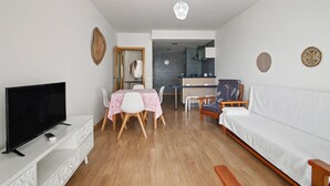 A modern living room with a flat-screen TV, a dining table with chairs, a sofa, and a kitchen area in the background. - Apartment 'Ocean Terrace 3 B - With Pool' with Swimming Pool and Balcony (Armação de Pêra)