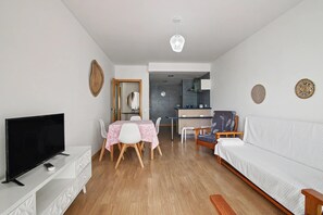 Ein modernes Wohnzimmer mit Flachbildfernseher, einem Esstisch mit Stühlen, einer Couch und einer Küchenzeile im Hintergrund.