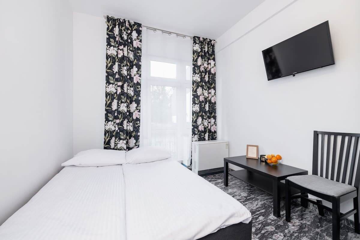 Ein Hotelzimmer mit Bett, Schreibtisch, Stuhl, Fernseher und Vorhängen mit Blumenmuster.