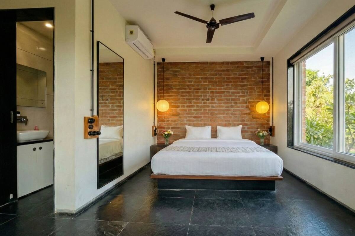 Ein modernes Schlafzimmer mit Backsteinwand, einem großen Bett, einem Deckenventilator und einem Fenster mit Blick auf Grünflächen.