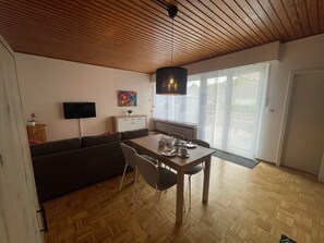 Een moderne woonkamer met een houten plafond, een eettafel met stoelen, een bank, een televisie en een schilderij.