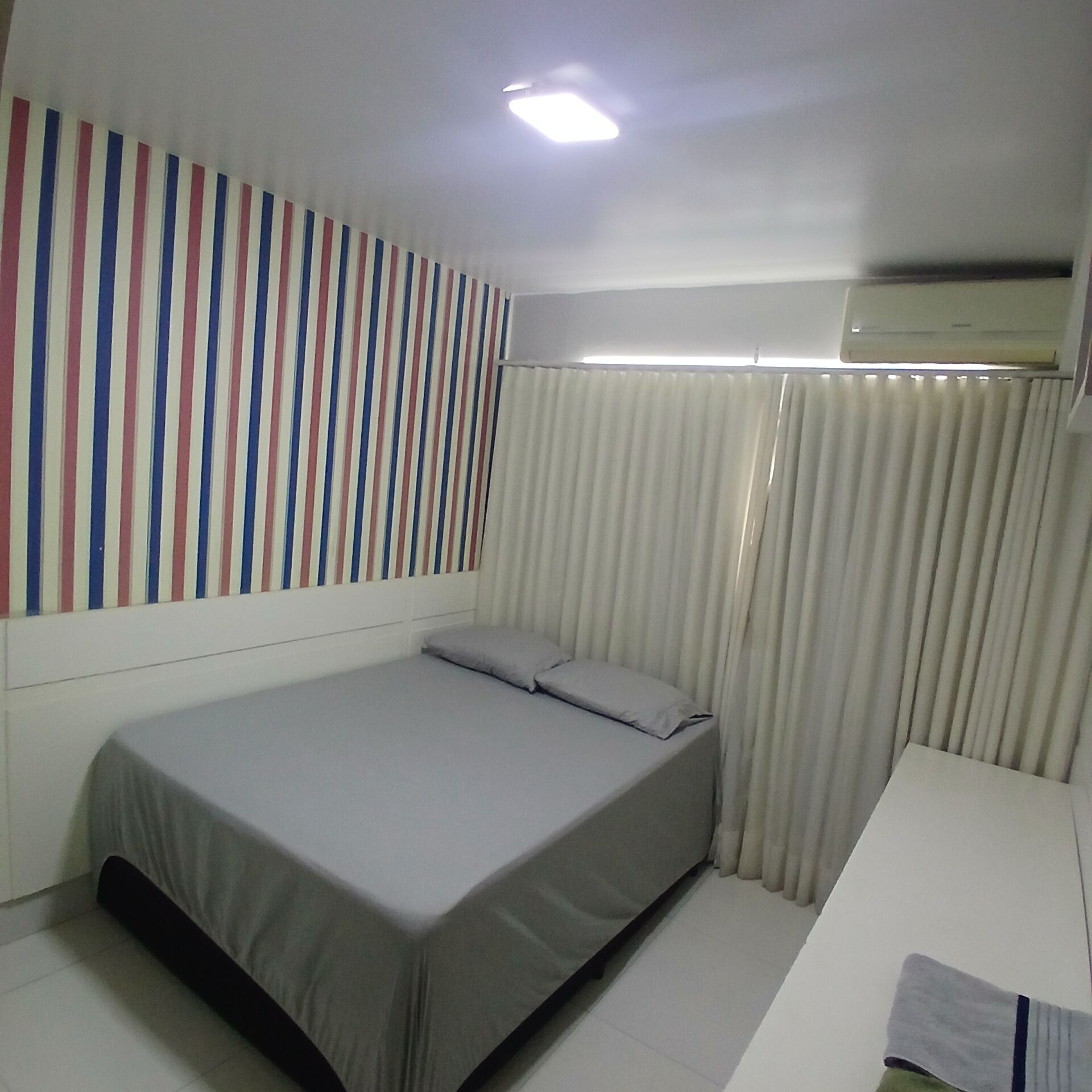 A small, neatly arranged bedroom with a single bed, a white desk, and a striped wall decoration.