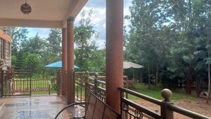 A covered outdoor area with a metal railing, a stone wall, and a view of a green landscape. - Casa Kalimbini Resort (Sultan Hamud)