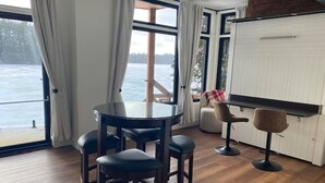Une pièce comprenant une table ronde et quatre chaises, un coin bar et de grandes fenêtres donnant sur l’eau.