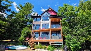 A multi-story building with a balcony, wooden deck, and a red roof. - Welcome to On Lake Time on beautiful Lac McGregor (Val-des-Monts)