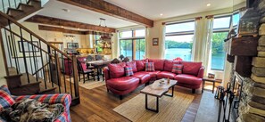 A spacious living area with a red leather sectional sofa, a wooden coffee table, and a kitchen with a large island. - Welcome to On Lake Time on beautiful Lac McGregor (Val-des-Monts)