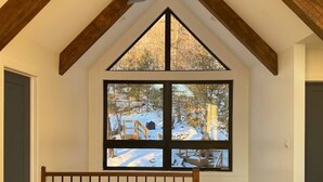 Une pièce aux plafonds hauts, dotée d’une grande fenêtre, de poutres en bois et d’un ventilateur de plafond.