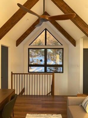A high-ceiling room with a large window, wooden beams, and a ceiling fan.