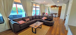 A modern living room with a sectional sofa, a coffee table, and a view of a lake through large windows. - Welcome to On Lake Time on beautiful Lac McGregor (Val-des-Monts)