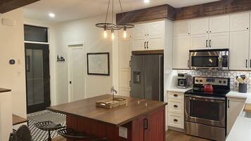 A modern kitchen with a central island, stainless steel appliances, and a wooden ceiling.