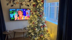 Uma sala de estar com árvore de Natal, uma televisão de tela plana e uma pequena mesa redonda.