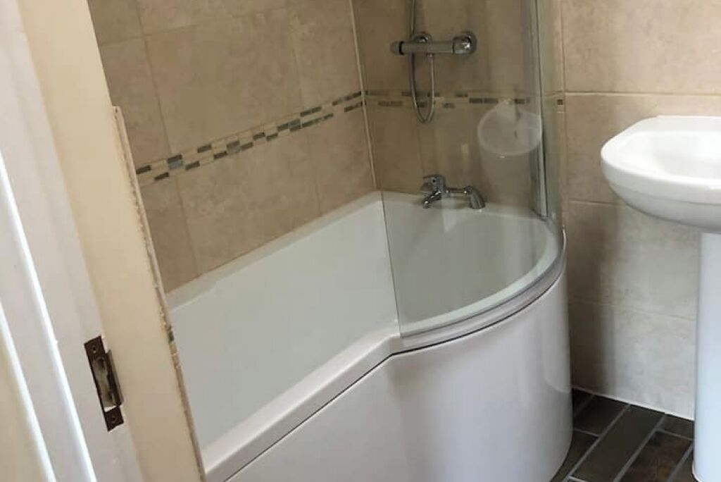 Un baño con bañera de hidromasaje con mampara de vidrio, un lavabo blanco y paredes con azulejos color beige.