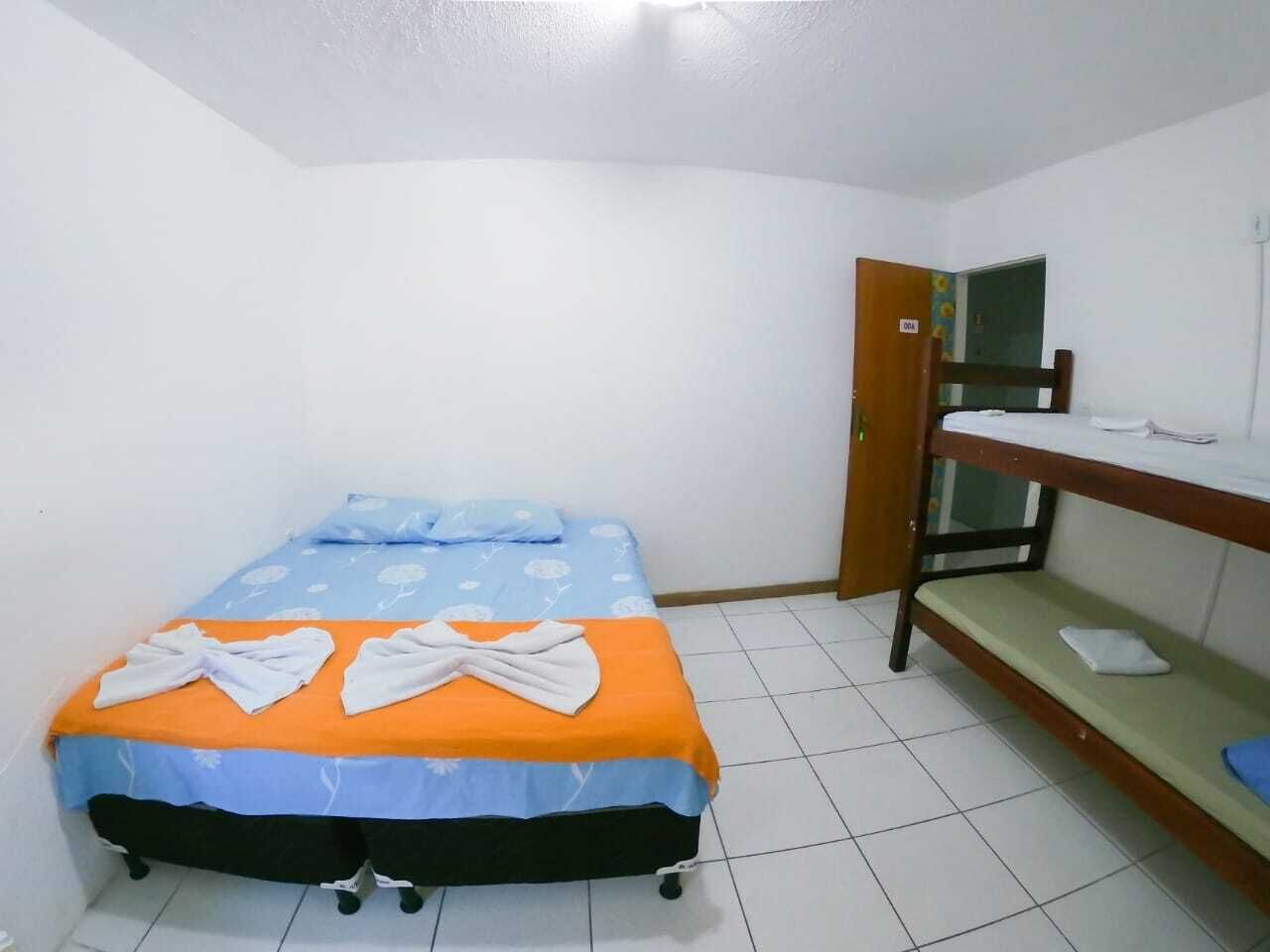 Una habitación pequeña con una cama individual y una litera contra la pared, suelo de baldosas y una puerta con el símbolo de número.