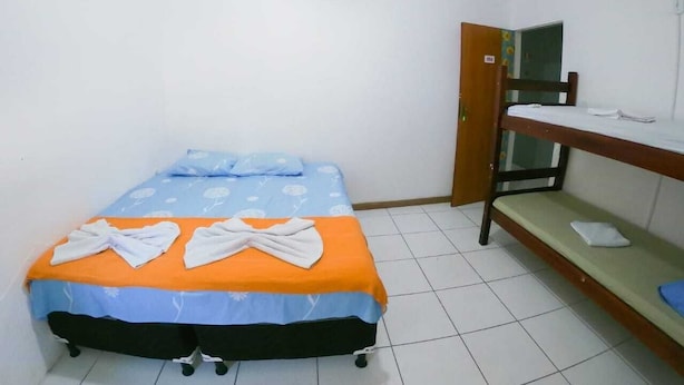 Une petite chambre avec un lit simple et un lit superposé adossé au mur, un sol carrelé et une porte portant un numéro.