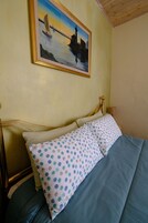 Un dormitorio con cama, cabecera de madera, cuadro enmarcado de un velero y mesita de noche con lámpara.