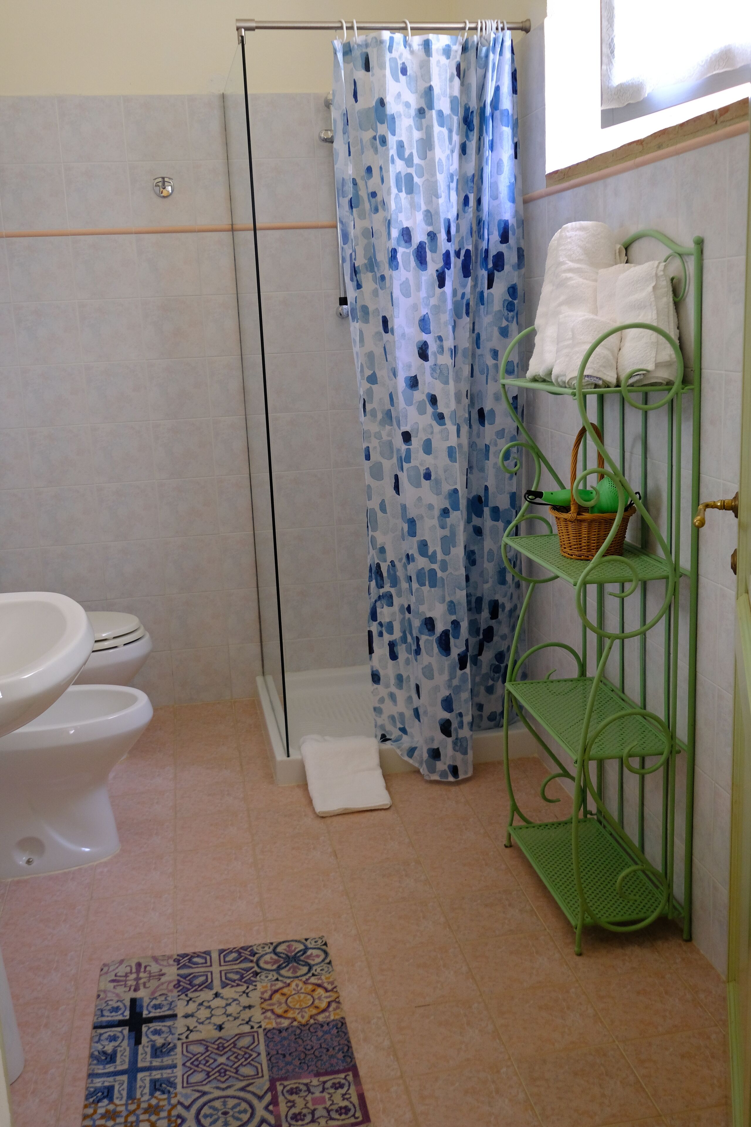 A bathroom with a shower, toilet, and a green metal rack with a basket.