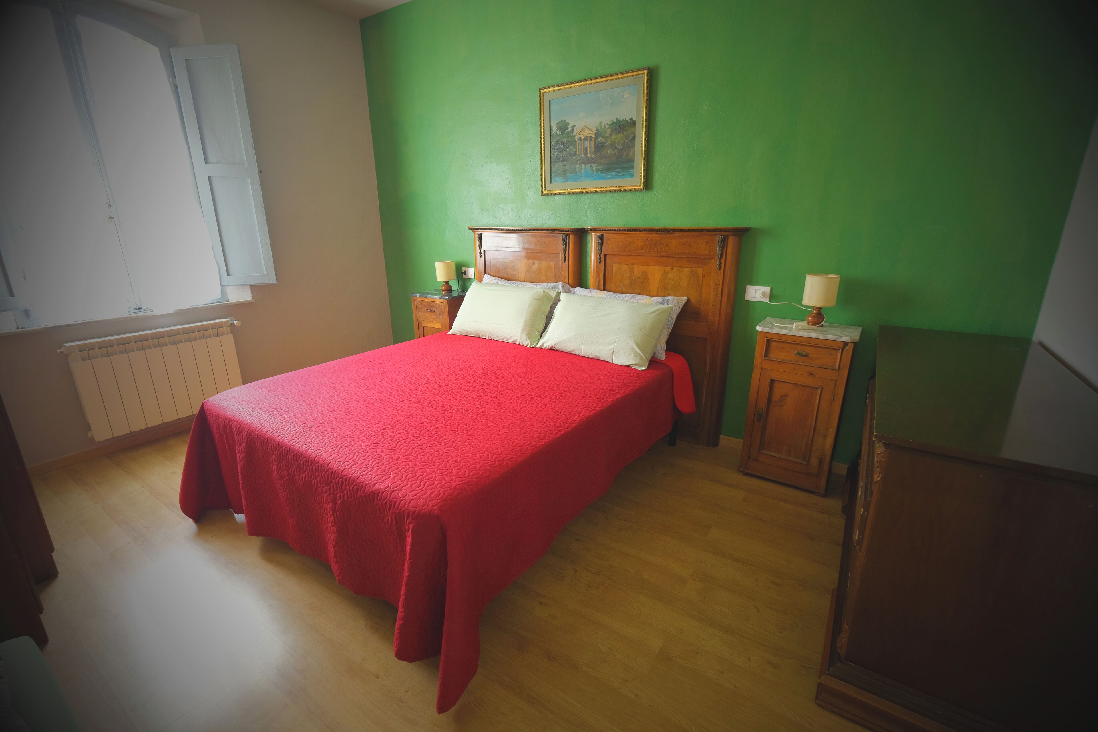 A bedroom with a wooden bed, green walls, and a window with white shutters.