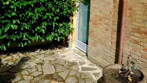Un patio empedrado con una planta en maceta, un muro de ladrillo y una puerta.