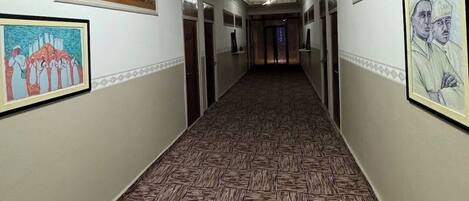 A hallway with patterned flooring, framed artwork on the walls, and a decorative ceiling with circular lights.