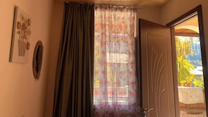 A room with a wooden ceiling, a door with a brass handle, a floral curtain, and a framed artwork on the wall.