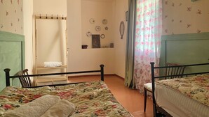 A bedroom with two beds, a wooden ceiling, floral wallpaper, and a window with floral curtains.