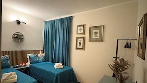 A hotel room with two beds, a bedside table, a potted plant, and wall-mounted artwork. - Gardaland & Lake Apt with parking lot (Cavalcaselle)