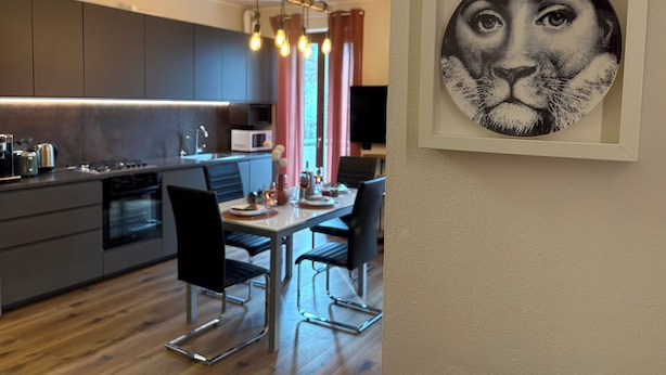 A modern kitchen with dark cabinets, a central island, and a dining area with two chairs and a table. - Gardaland & Lake Apt with parking lot (Cavalcaselle)