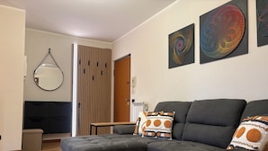 A modern living room with a sectional sofa, a round mirror, and abstract wall art. - Gardaland & Lake Apt with parking lot (Cavalcaselle)
