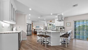 A modern kitchen with a central island, bar stools, and a view of the outdoors. - Beach Daze: Island Style Charm on Canal, Quick Walk to Beach! (Sanibel)
