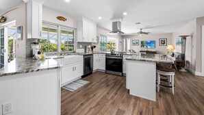 A modern kitchen with white cabinetry, a central island, and a view of the outdoors. - Beach Daze: Island Style Charm on Canal, Quick Walk to Beach! (Sanibel)
