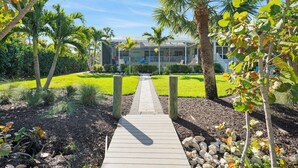 A pathway leading to a building with a modern design, surrounded by a well-maintained garden with palm trees and shrubs. - Beach Daze: Island Style Charm on Canal, Quick Walk to Beach! (Sanibel)