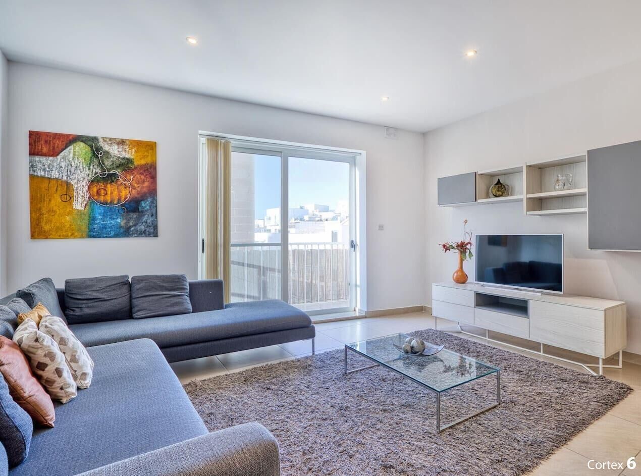 Un salon moderne avec un canapé gris, une table basse en verre et un téléviseur à écran plat posé sur un meuble blanc.