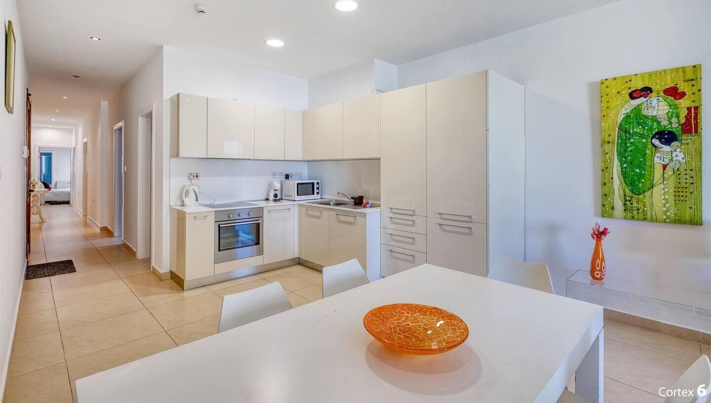 Une cuisine moderne avec des meubles blancs, un four à micro-ondes et une cuisinière. On y trouve une table à manger avec un bol décoratif placé au premier plan.