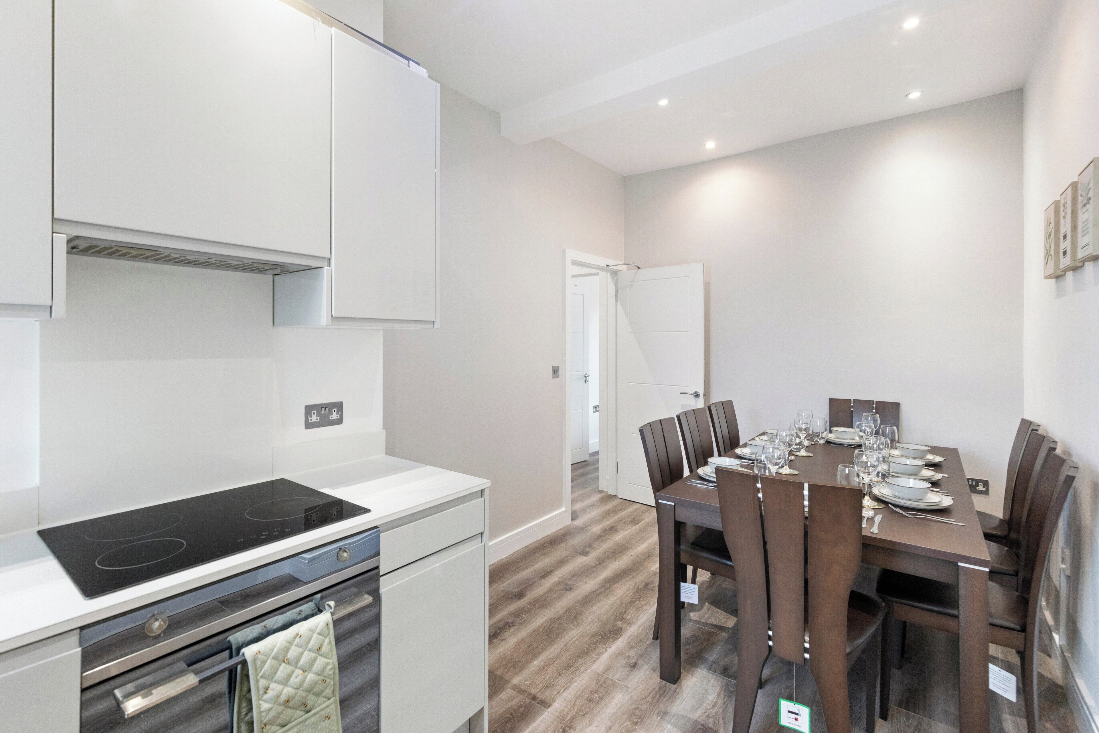A modern kitchen with white cabinetry, a black induction cooktop, and a dining area with a wooden table and chairs.