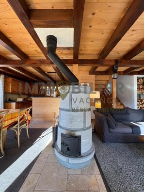 Ein modernes Interieur mit Kamin aus Stein, Holzbalken, Essbereich und einer Sitzecke.