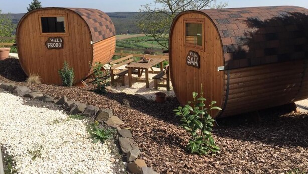 Twee houten hutten met de namen 'Villa Frodo' en 'Villa Sam', een picknicktafel en uitzicht over het landschap.