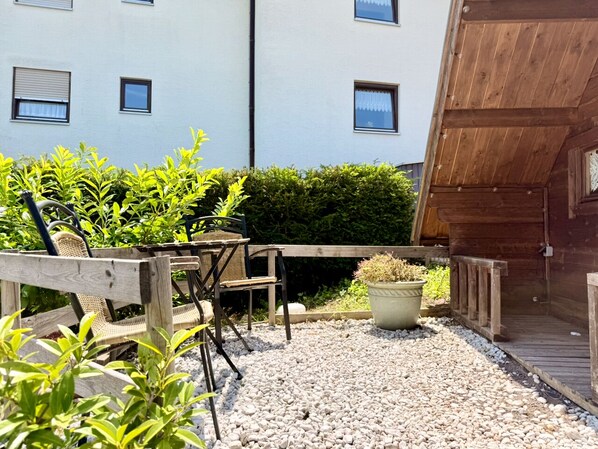 A patio area with a wooden table and chairs, surrounded by gravel and potted plants. - Apart-Hotel Kastanienhof (Dannenfels)