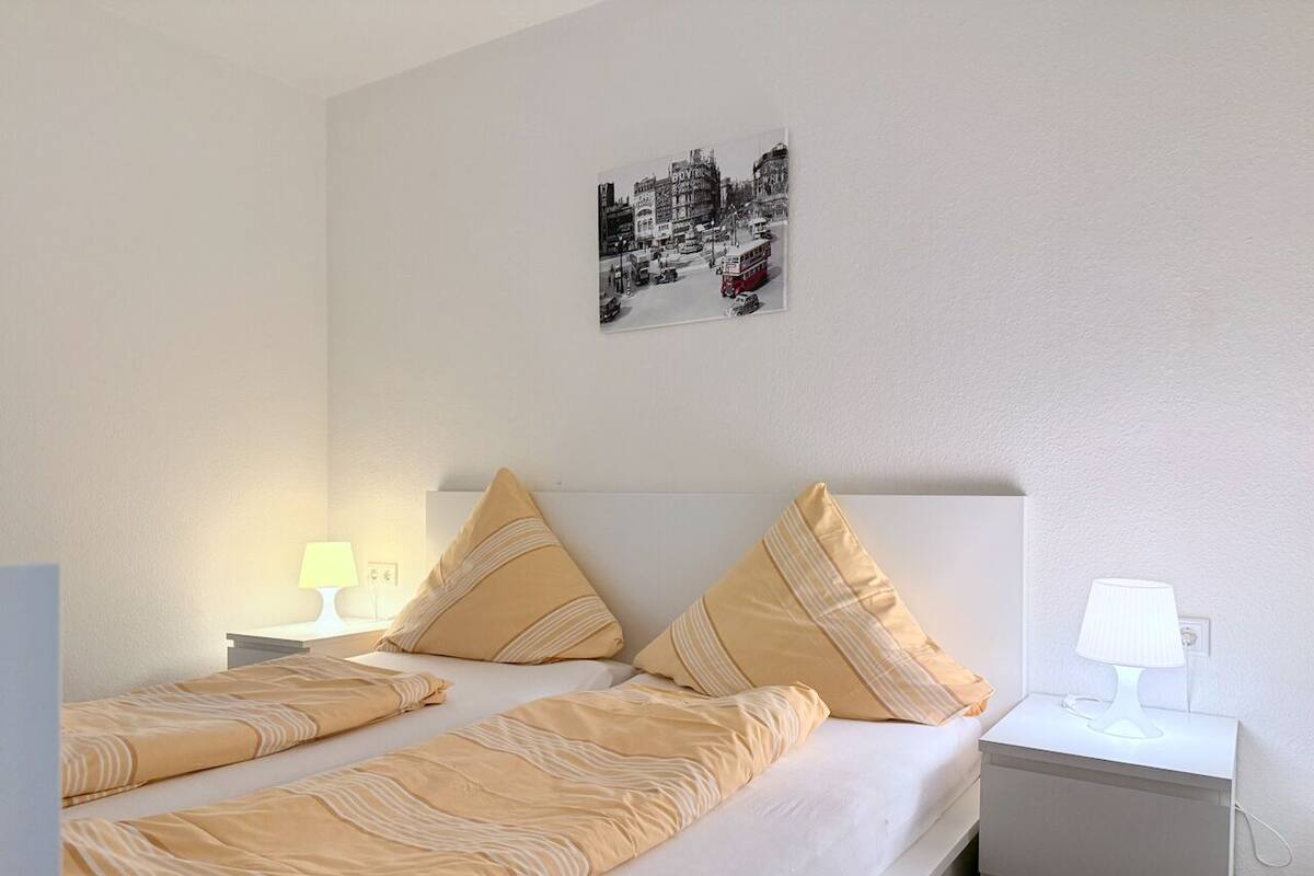 Ein Doppelbett mit zwei Kissen, ein Nachttisch mit Lampe und ein Wandbild.