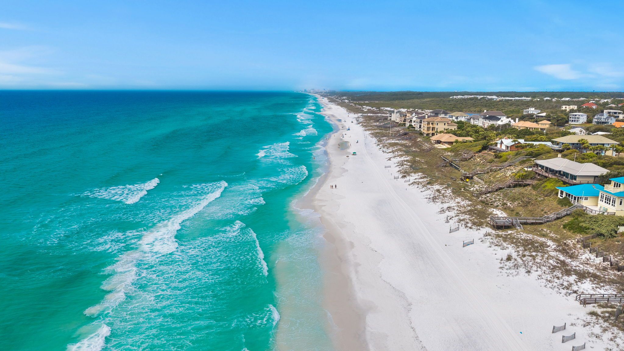 A coastal beach with a clear view of the ocean, a sandy shoreline, and residential buildings.