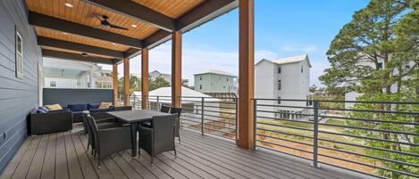 En overdækket terrasse med et bord, stole, en sofa og udsigt til nabolagets huse.