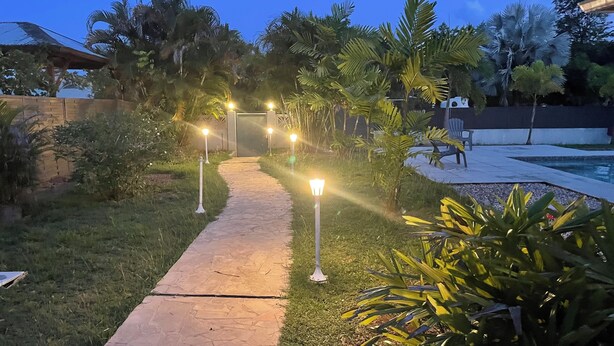 Un sendero iluminado que conduce a una zona de piscina, rodeada de abundante vegetación y palmeras.