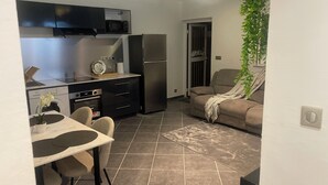 Una cocina compacta equipada con microondas, horno y refrigerador. Hay una mesa de comedor con sillas y una planta en maceta. Un sofá se encuentra en la sala con una manta.
