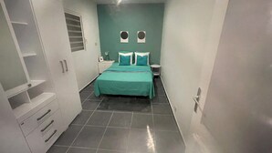 Una habitación de hotel estrecha con una cama, una mesita de noche y un armario.